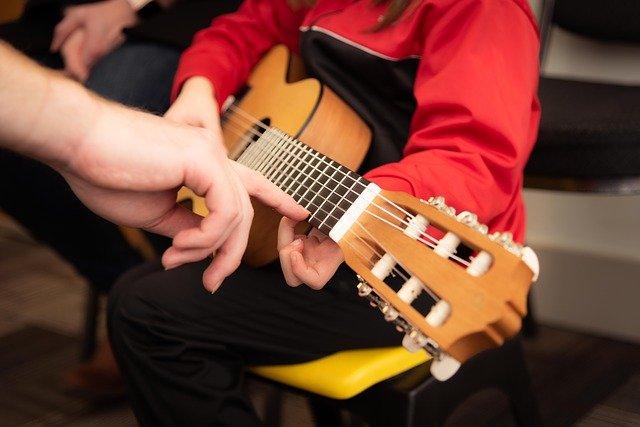 Image of a music teacher showing a student how to play the guitar